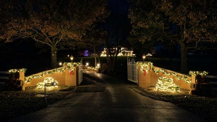 Driveway entry walls and trees trimmed with warm white lights at night
