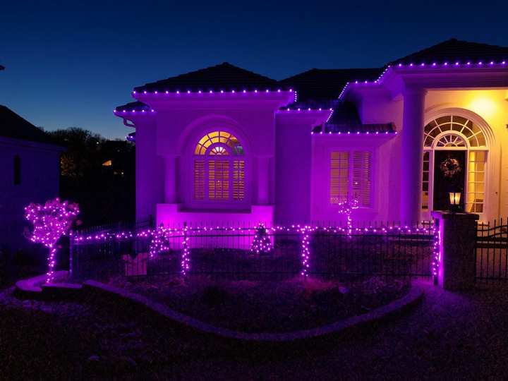 Stucco home lit in purple, with purple lights along the roofline and front fence