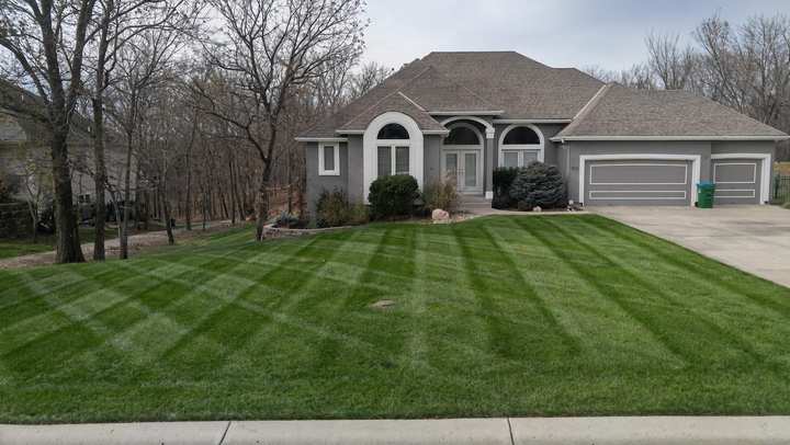 Striped, leaf-free front lawn in front of a stone and stucco home with a three-car garage on an overcast fall day
